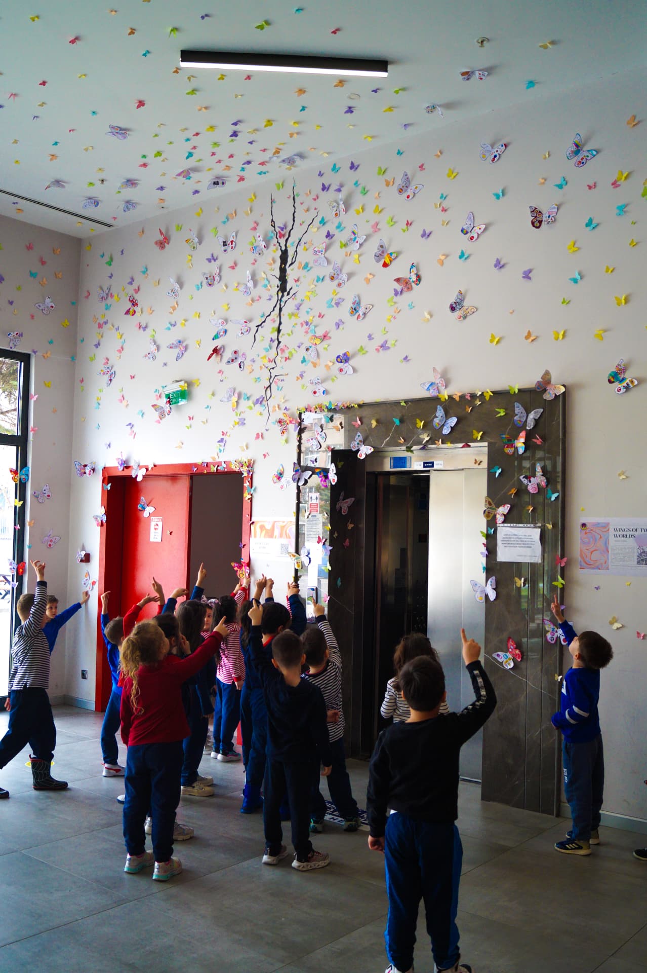 Children pointing up at hundreds of handmade paper butterflies covering the school walls and ceiling