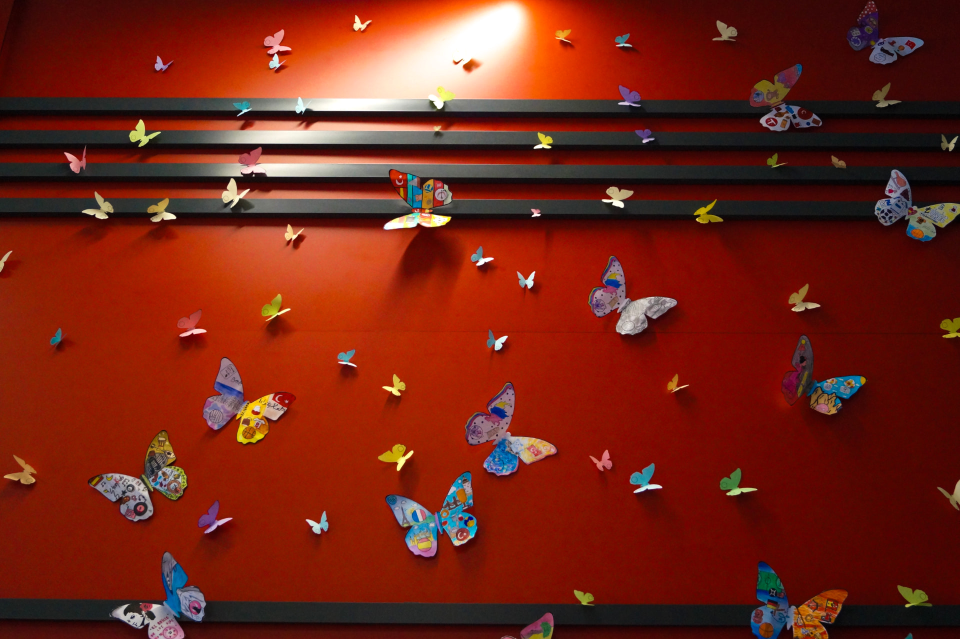 Close view of individually decorated paper butterflies on a deep red wall