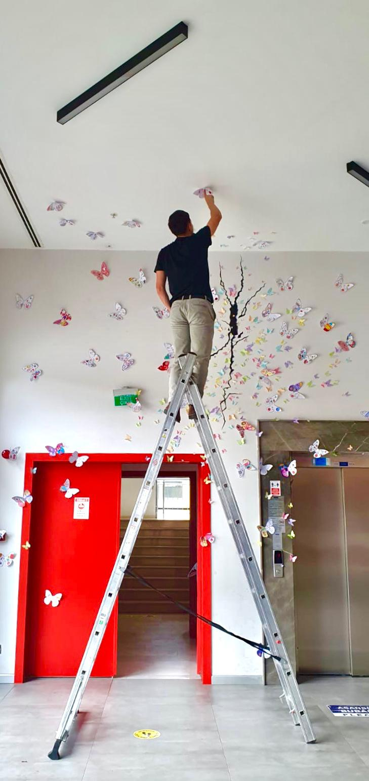 A teacher on a ladder placing butterflies on the ceiling